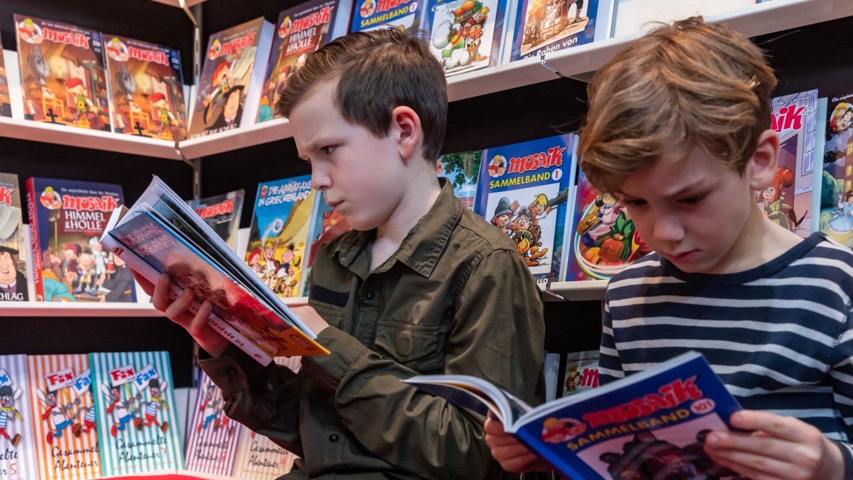 zwei Jungen lesen Comics vor einem Buchregal gefüllt mit Mosaik Büchern auf der Leipziger Buchmesse 2019