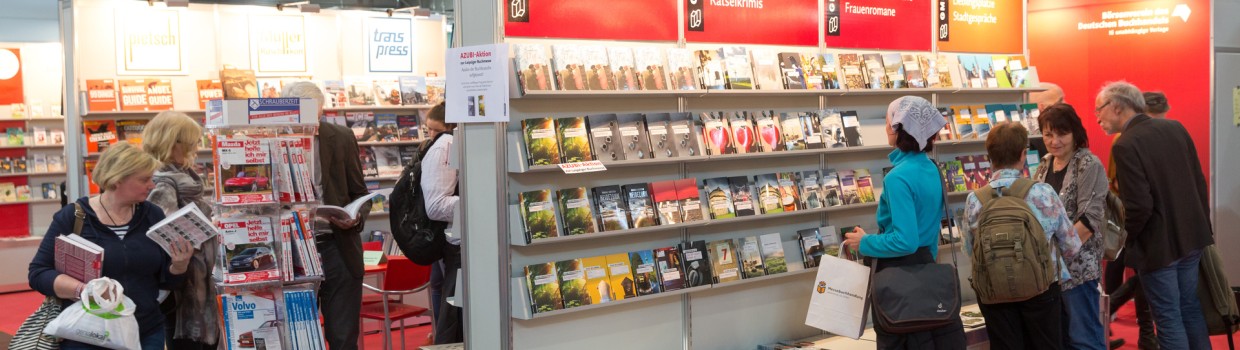 Besucher:innen der Leipziger Buchmesse 2017 stehen vor Bücherregalen und blättern teilweise in Heften oder Büchern. Über dem Regal sind die verschiedenen Genres abgebildet. 