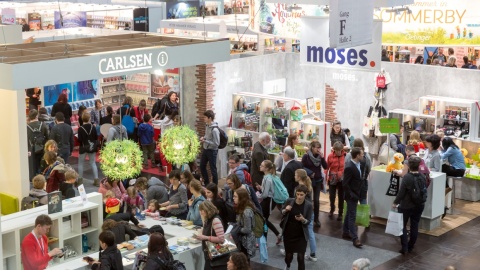Viele Besucher:innen tümmeln sich um verschiedene Messestände. Man schaut von schräg oben auf die Menschen, es erinnert an eine Vogelperspektive. 