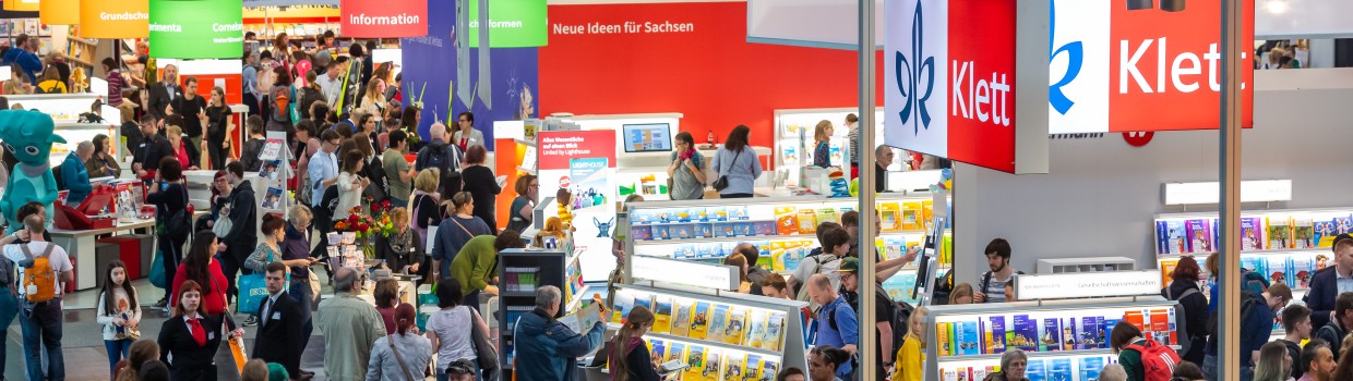 Besucher:innen und Messestände von veschiedenen Verlagen in der Halle auf der Leipziger Buchmesse.