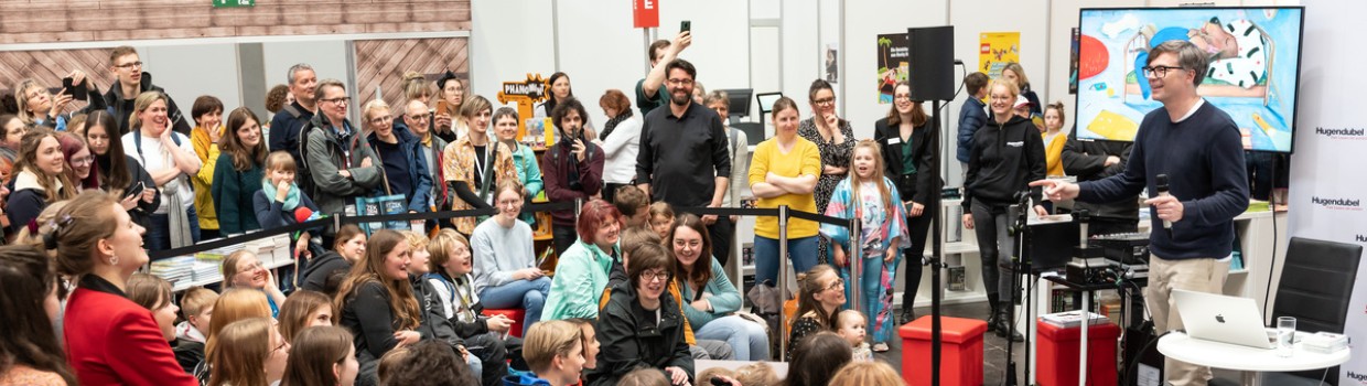 Zahlreiche Kinder und Jugendliche verfolgen eine Lesung in der Messe-Kinderbuchhandlung von Hugendubel. 