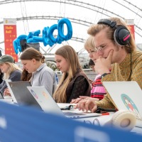 an einem langen Tisch sitzen Podcaster:innen auf der Leipziger Buchmesse 2023 und arbeiten an ihren Laptops