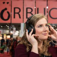 Junge Frau mit Kopfhörer auf der Leipziger Buchmesse vor einem großen Schild mit der Aufschrift "Hörbuch"