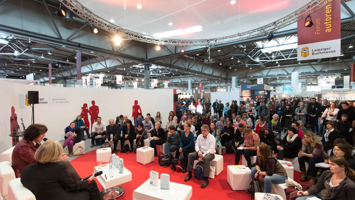 Die autoren@leipzig Bühne von 2016. Links im Vordergrund sprechen zwei Personen ins Mikrofon. Ihnen gegenüber sitzen viele Zuhörende auf Hockern und dem Boden. 