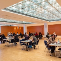 Eine Veranstaltung auf der Leipziger Buchmesse im Congress Center Leipzig. Im Raum stehen mehrere Tische an denen verschieden viele Personen sitzen. 