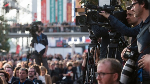 Ein Foto von einer Veranstaltung auf der Leipziger Buchmesse. Zu sehen sind drei Kameramänner und deren Kameras, welche auf ein Objekt außerhalb des Bildes gerichtet sind. Zwei der Männder sind scharf rechts im Bild zu sehen. Einer ist im Hintergrund verschwommen abgebildet. 