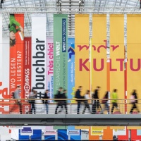 Glashalle der Leipziger Buchmesse 2023 mit vielen von der Decke hängenden Werbebannern und vorbeilaufenden Besucher:innen