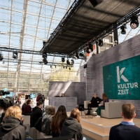 Die Kultur Zeit Bühne auf der Leipziger Buchmesse 2023 bei einem Talk mit 2 Personen vor vollbesetztem Publikum in der Glashalle