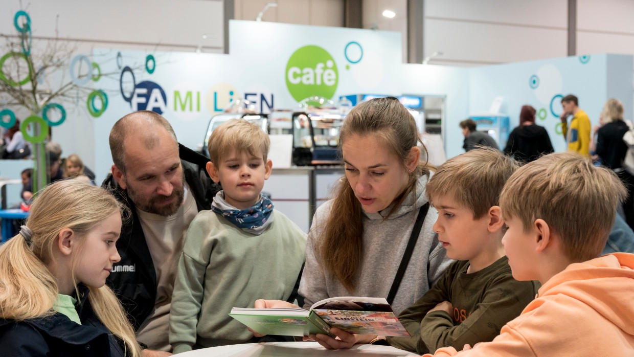 Eine Familie mit Mutter, Vater und 4 Kindern im Familiencafé der Leipziger Buchmesse. Die Mutter liest aus einem Kinderbuch vor.