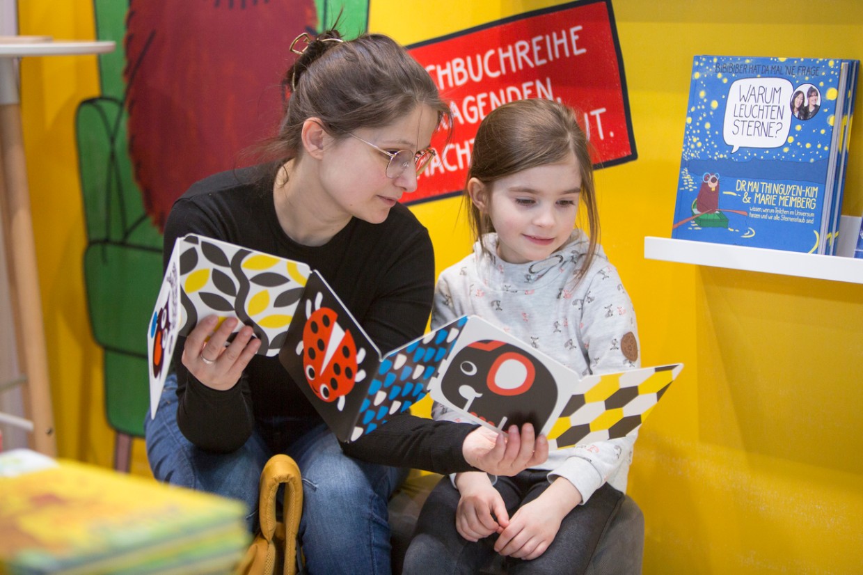 Frau und Mädchen lesen gemeinsam ein Bilderbuch auf der Leipziger Buchmesse 2024