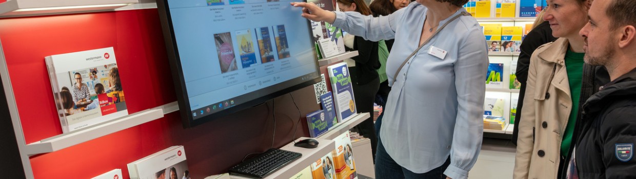 Frau demonstriert Besucher:innen das digitale Unterrichtssystem an einem Bildschirm auf der Leipziger Buchmesse 2024