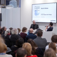 Bühnengespräch mit 2 Teilnehmer:innen auf der Bühne vom Medienforum vor vollbesetztem Publikum auf der Leipziger Buchmesse 2024