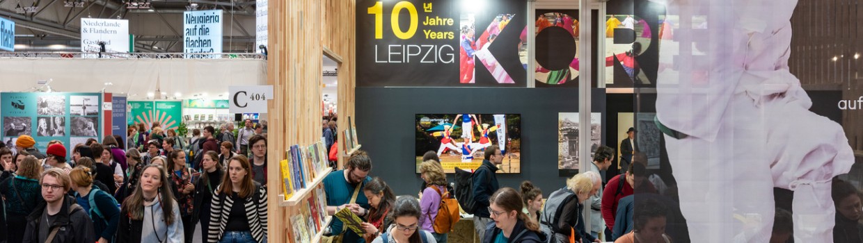 Ausstellungshalle mit koreanischem Messestand und italienischer Flagge während der Leipziger Buchmesse 2024 mit viele Besucher:innen an Messeständen