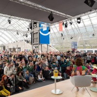 Innenaufnahme der Glashalle der Leipziger Messe mit vielen Besucher:innen aus der Perspektive der Medienbühne während der Leipziger Buchmesse 2024