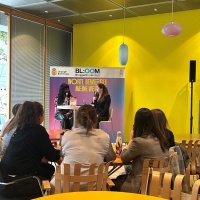 2 Blogger:innen unterhalten sich an einem Tisch, mehrere Zuschauer:innen hören ihnen zu 