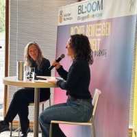 2 Bloger:innen unterhalten sich im Blogger Room der LBM an einem Tisch mit Mikros in der Hand 