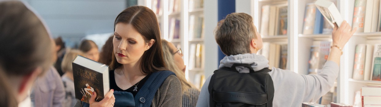 Eine Frau liest stehend in einem Buch vor einen großen Buchregal auf der Leipziger Buchmesse 2025