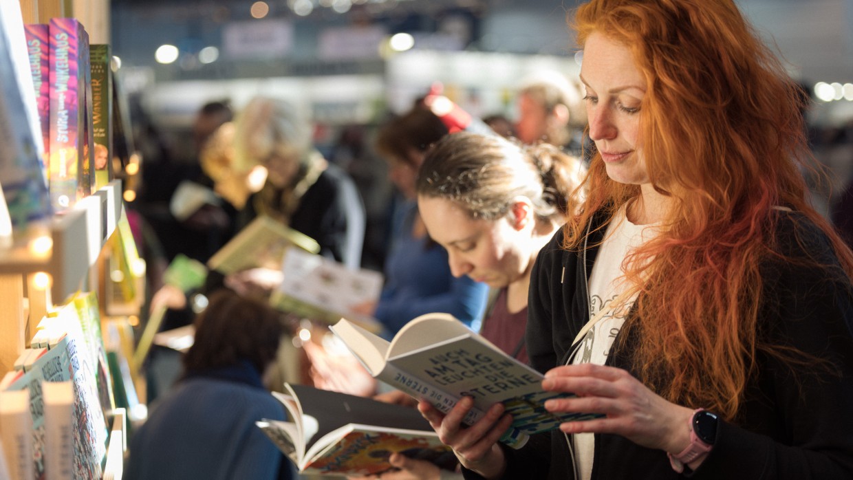 Frau mit roten lockigen Haaren liest aus einem Buch auf der Leipziger Buchmesse 2025