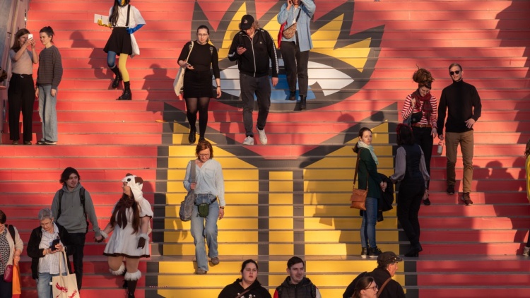 Besucher:innen laufen Treppe herunter, auf der das Logo der Leipziger Buchmesse 2025 drauf ist