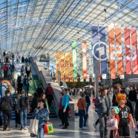 Impression der Glashalle mit vielen Besucher:innen und bunten Fahnen auf der Buchmesse 2025