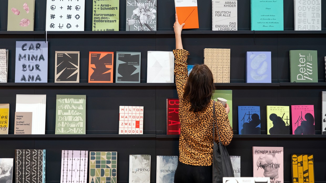 Besucherin der Leipziger Buchmesse 2025 nimmt ein Buch aus einer Wand mit ausgestellten Büchern