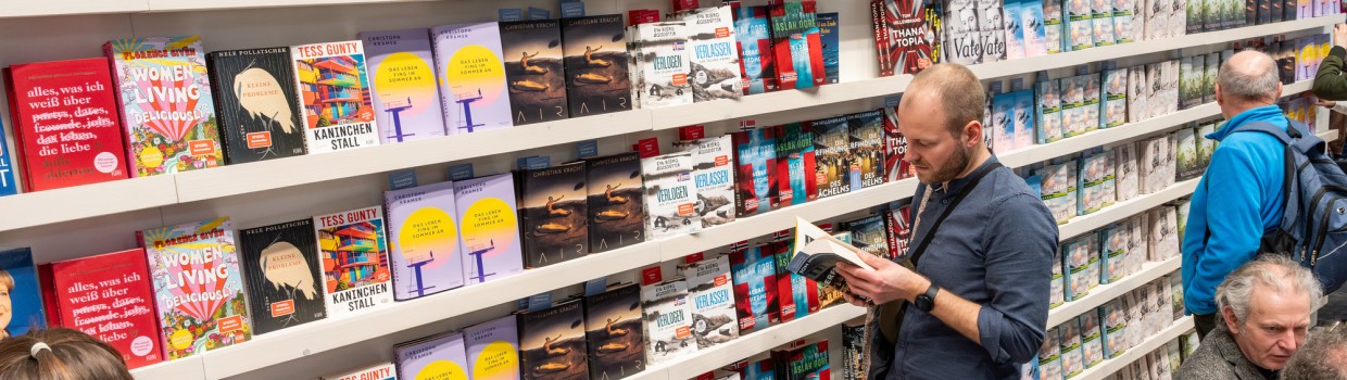 Ein Mann liest stehend in einem Buch vor einen großen Buchregal auf der Leipziger Buchmesse 2025