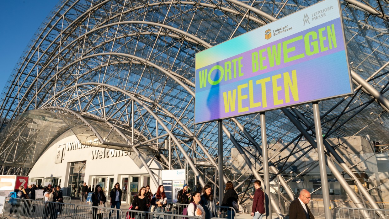 Glashalle der Leipziger Messe von außen bei sonnigem Wetter während der Leipziger Buchmesse 2025 mit großer LED-Bildschirmanzeige "Worte bewegen Welten"