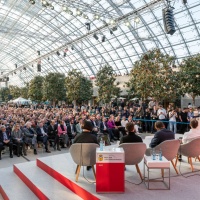 Blick von hinter der Bühne auf die Preisträger:innen und Moderator:innen bei der Verleihung des Preises der Leipziger Buchmesse 2025, Publikum im Hintergrund.