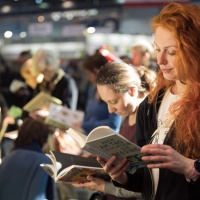 Frau mit roten lockigen Haaren liest aus einem Buch auf der Leipziger Buchmesse 2025