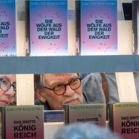 Eine Frau und ein Mann gucken durch ein Bücherregal auf der Buchmesse 2025