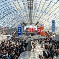 Innenansicht von der Glashalle der Leipziger Messe mit bunten Bannern und vielen Besucher:innen bei der Leipziger Buchmesse 2025