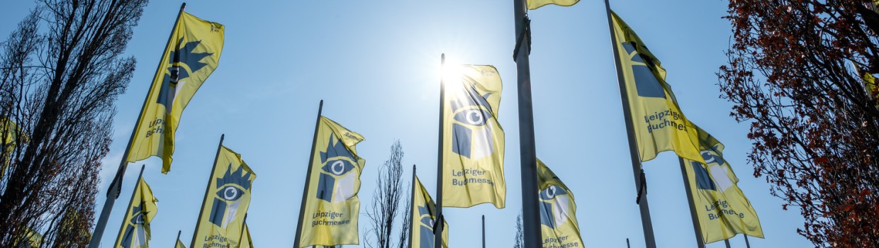 Gelbe Fahnen der Leipziger Buchmesse 2026 wehen vor blauem Himmel auf dem Messegelände