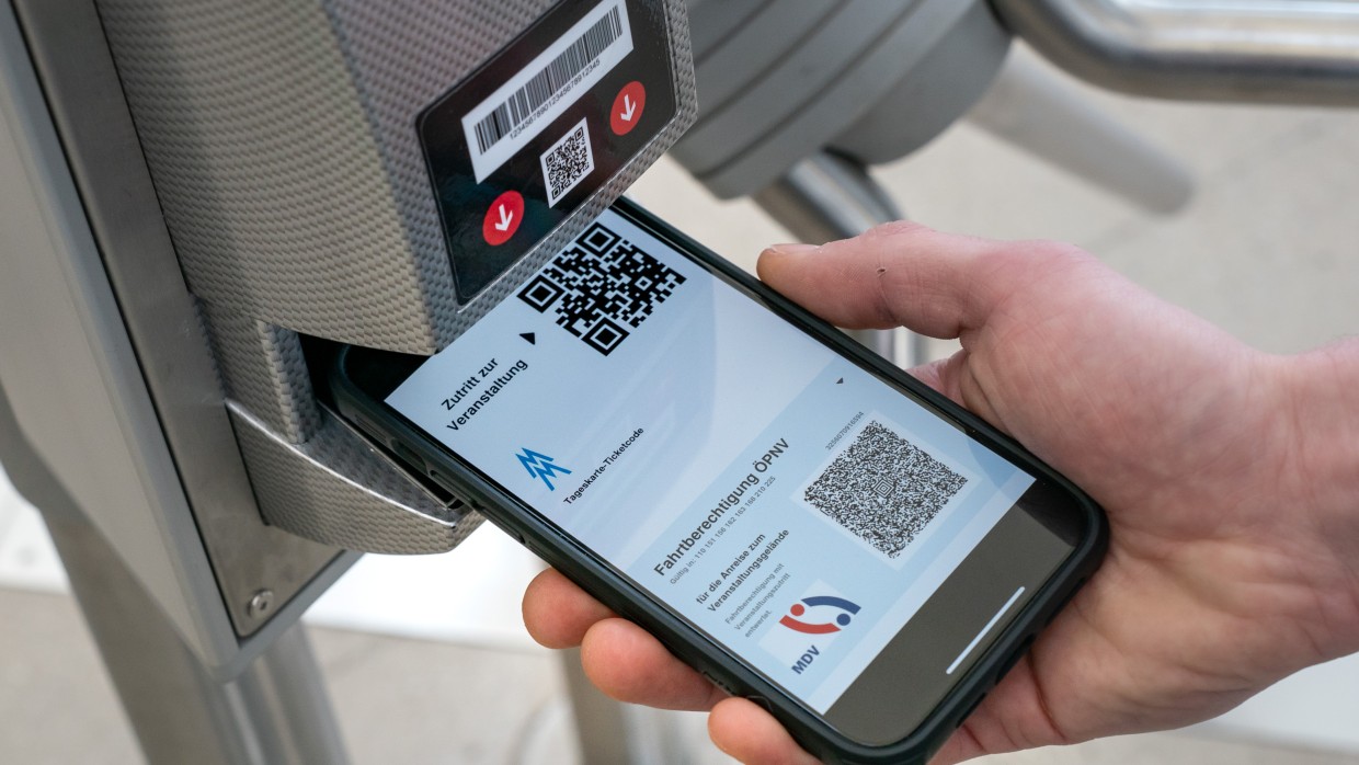 Eine Hand hält ein Smartphone unter den Scanner am Einlass-Drehkreuz. Auf dem Display ist ein elektronisches Ticket der Leipziger Messe mit QR-Code zu erkennen inkl. ÖPNV-Ticket.