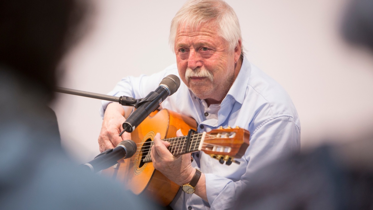 Older man plays guitar on stage at the Forum Die Unabhängigen at the Leipzig Book Fair 2024