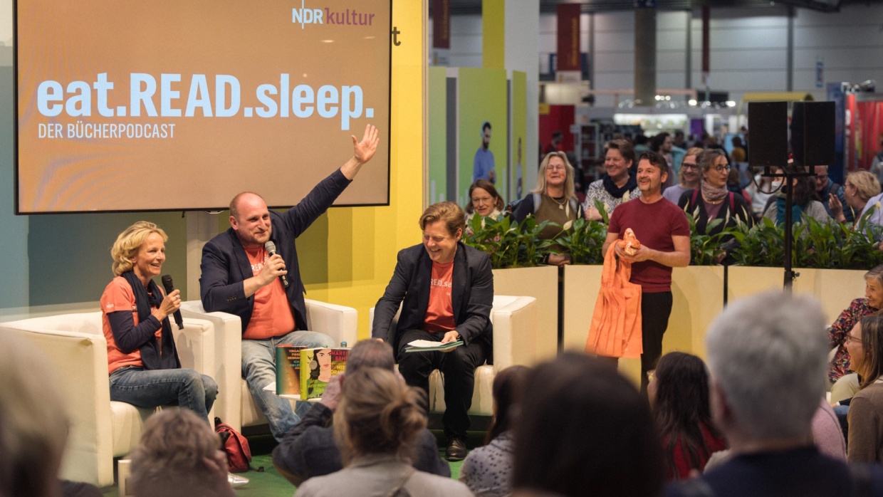 Stage event of the podcast "eat.read.sleep." with several people in the audio world of the 2025 Leipzig Book Fair in front of a full audience
