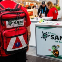 one member of the Awareness Team SAM of the Leipzig Book Fair 2025 walks past the booth, with the team’s red backpack clearly visible
