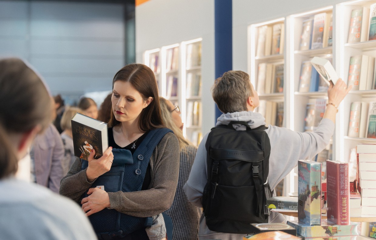 A woman stands reading a book in front of a large bookcase at the Leipzig Book Fair in 2025.