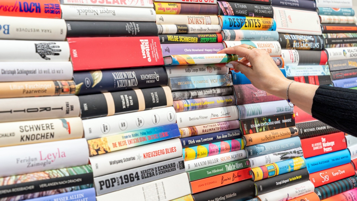 A woman's hand pulls a book from a large colorful stack of books at the Leipzig Book Fair in 2025