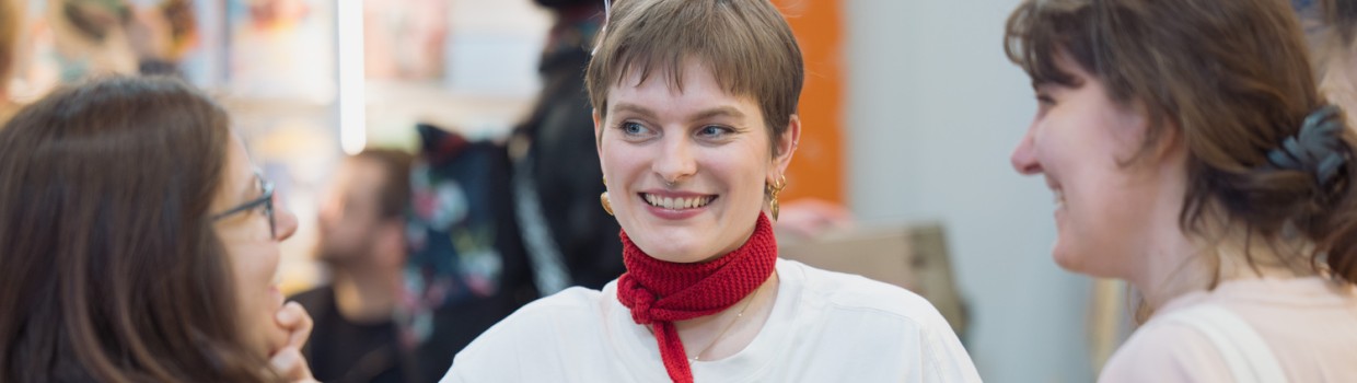 Exhibitor talking to two visitors at a book fair booth during Leipzig Book Fair 2026, one smiling at center