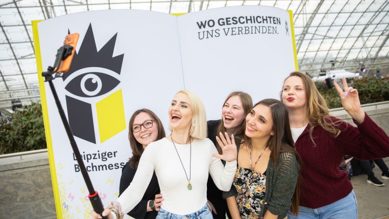 Five young female visitors take a selfie in front of a large book fair display at Leipzig Book Fair 2026