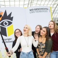 Five young female visitors take a selfie in front of a large book fair display at Leipzig Book Fair 2026
