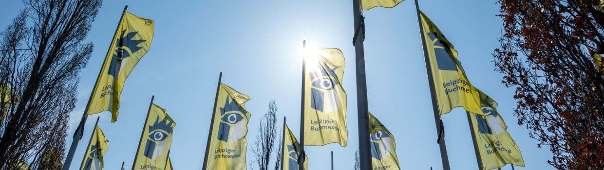 Yellow Leipzig Book Fair 2026 flags wave against a blue sky at the exhibition grounds