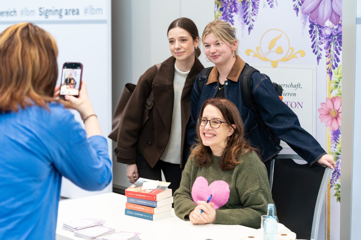 Author Julia Quinn poses with two visitors at a signing table as a photo is taken at Leipzig Book Fair 2026