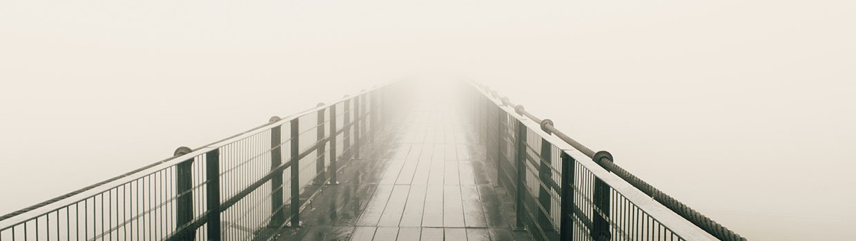 schwarz-weiß Fotografie einer Brücke, deren Ende von Nebel umhüllt ist