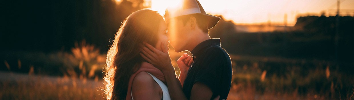 Zwei junge Personen stehen küssend auf einem Feld im Sonnenuntergang