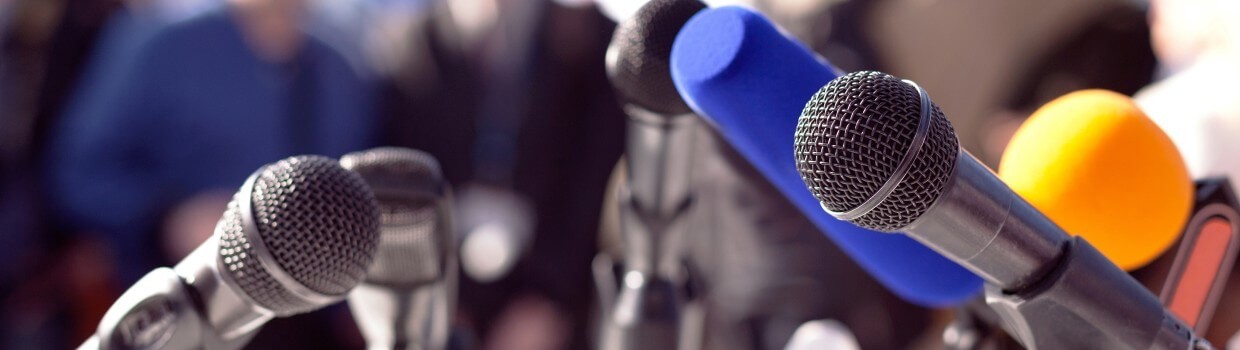 Ein Foto von verschiedenen Mikrofonen, es erinnert an die Mikrofone auf einer Pressekonferenz.