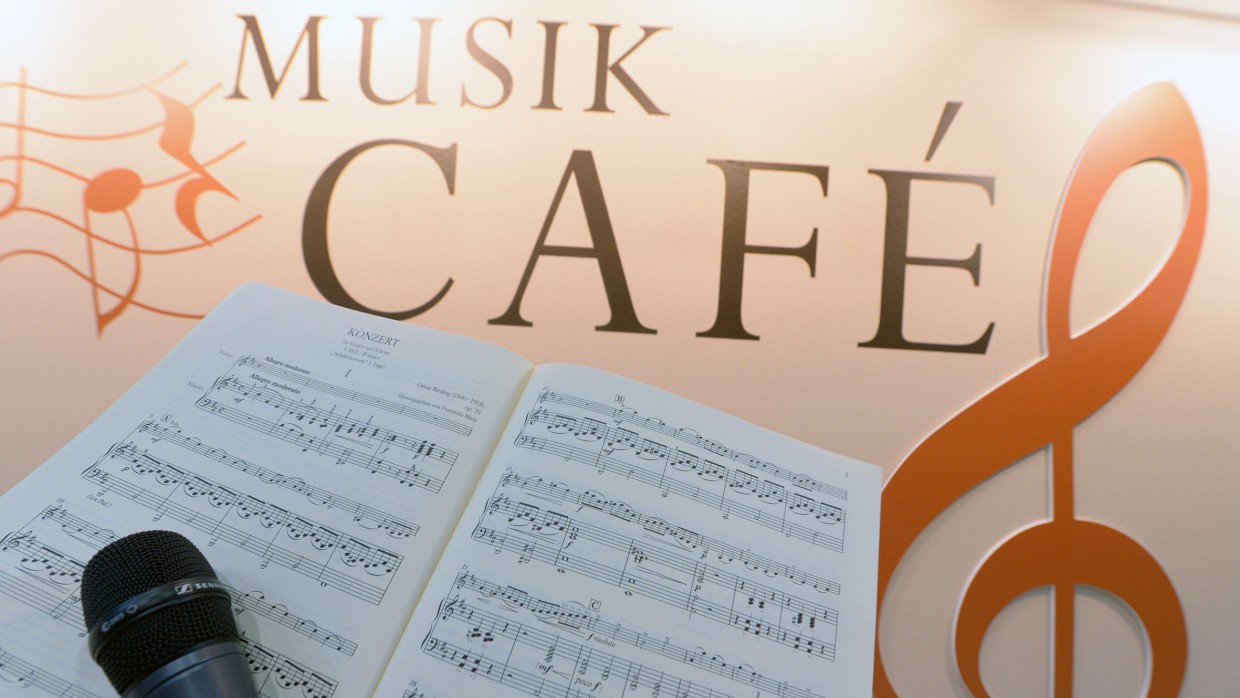 Ein Notenheft und ein Mikrofon im Vordergrund. Im Hintergrund eine Wand mit der Aufschrift: Musik Café. 
